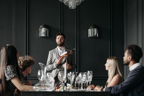 Free Group of adults attentively listening to a man presenting wine in a classy indoor setting. Stock Photo