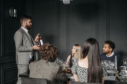 Free Sommelier presenting wine to a group of adults at a sophisticated indoor wine tasting event. Stock Photo