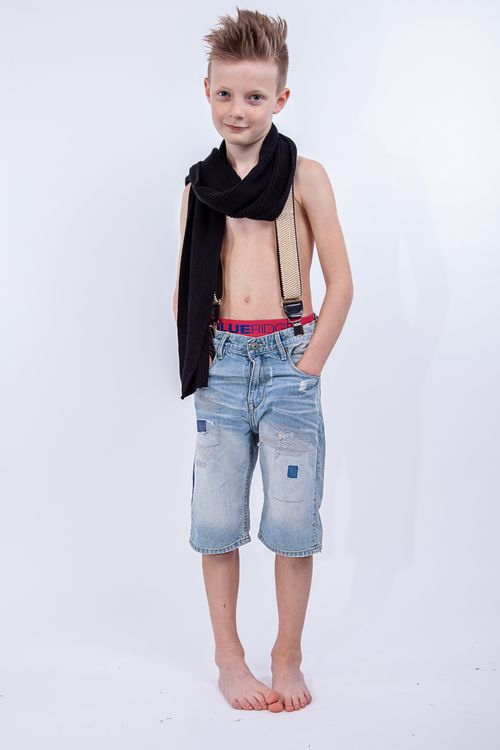 Free Young boy in denim shorts and suspenders posing with confidence, wearing a black scarf. Stock Photo