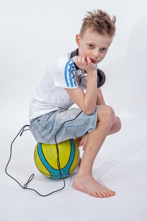 Free Boy sitting on a ball with headphones around his neck, capturing a casual and thoughtful moment. Stock Photo