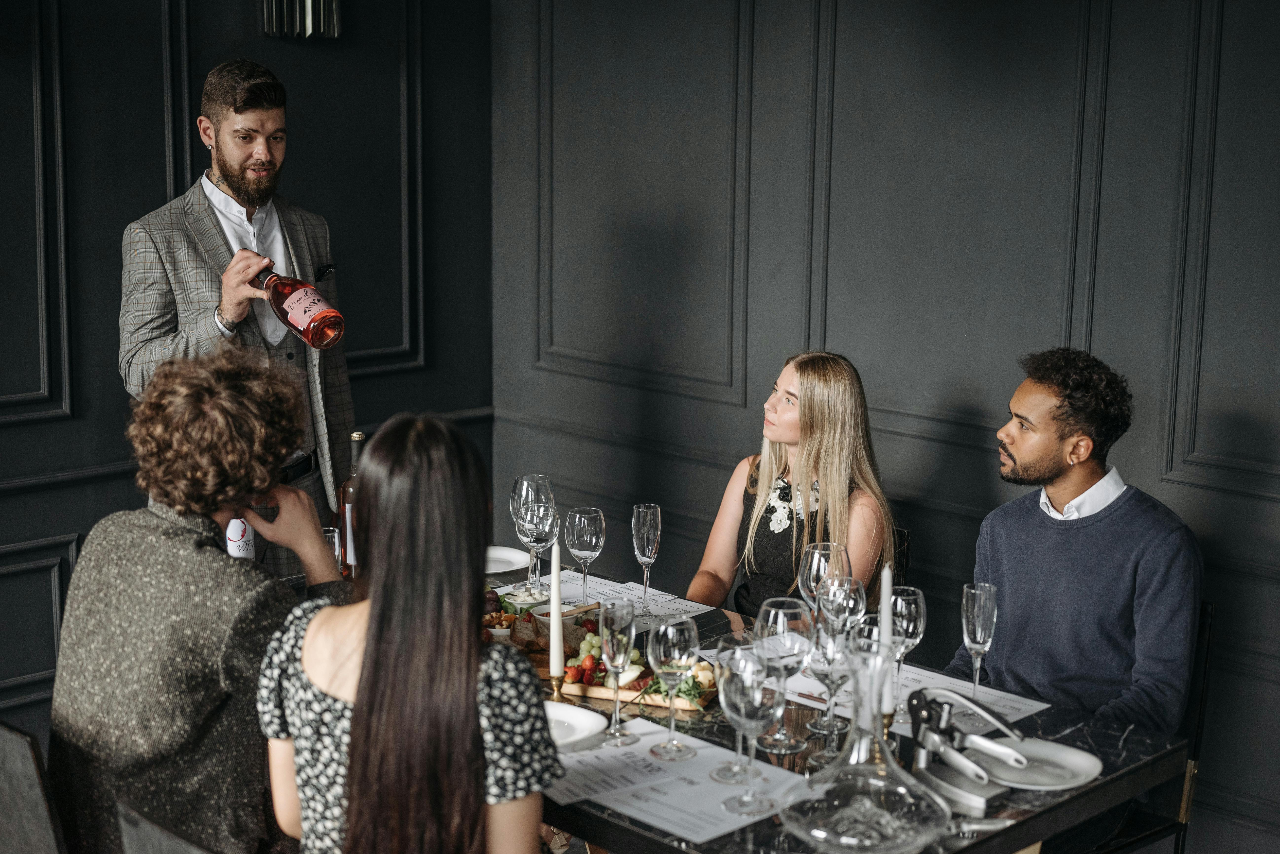 A sommelier presents wine to a group of friends in a sophisticated setting, enhancing their dining experience.