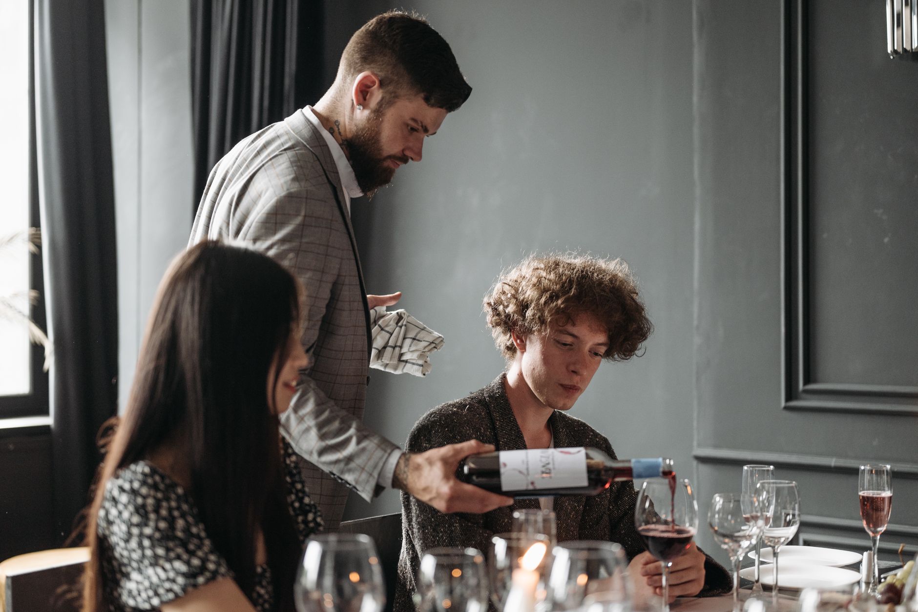A sommelier serves wine to guests at an elegant dinner party indoors.