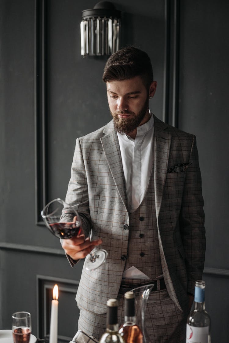 A Man In Plaid Suit Looking At The Glass Of Red Wine He Is Holding