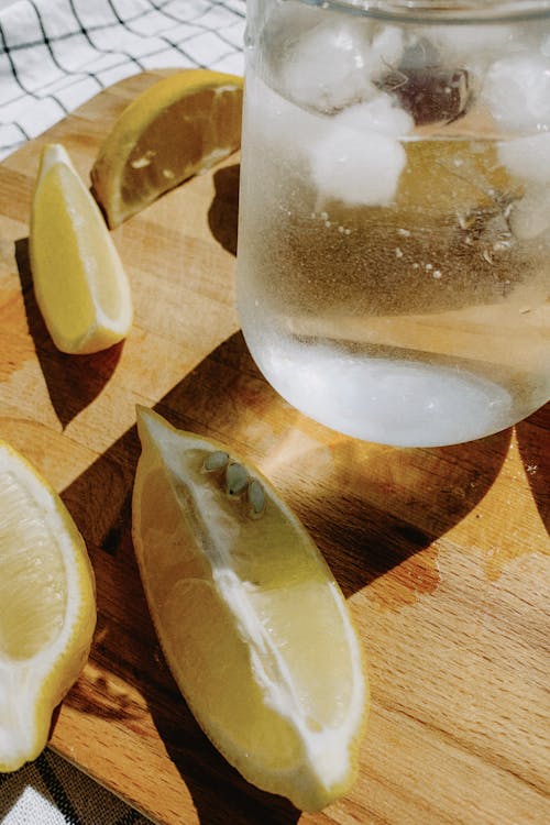 Sliced Lemon on Brown Wooden Chopping Board with a Glass of Ice Water