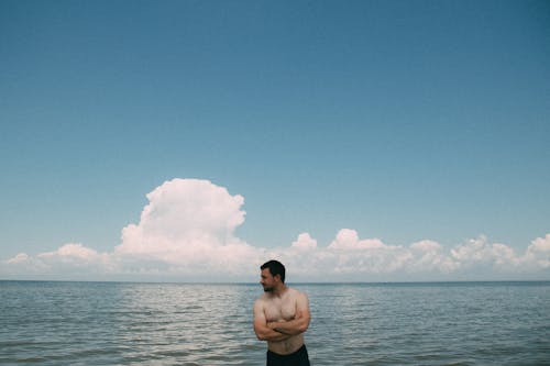 Man in Black Shorts Standing on Seashore Under Blue Sky