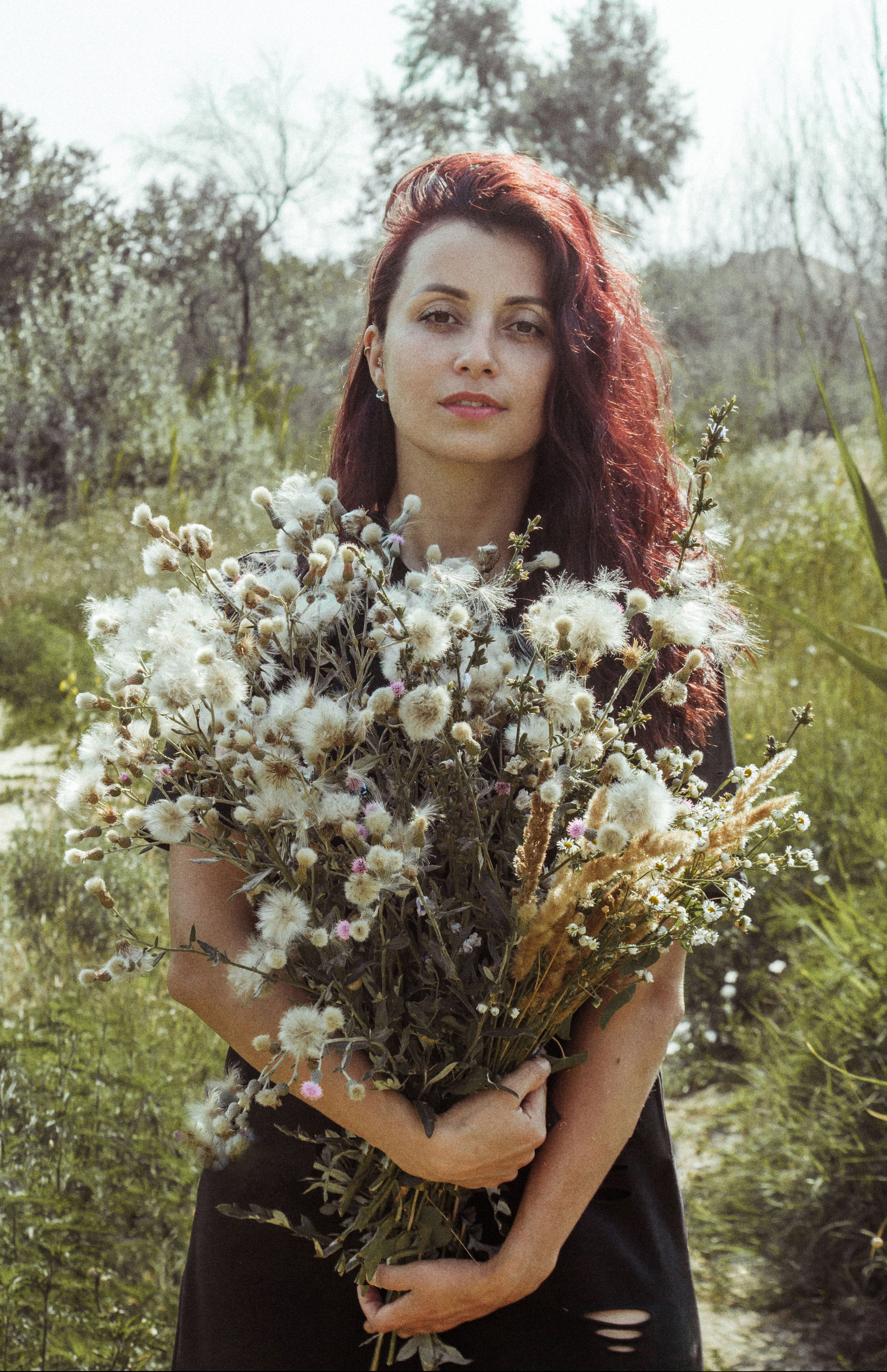 Woman with red hair holding a wildflower bouquet in a sunny outdoor setting.