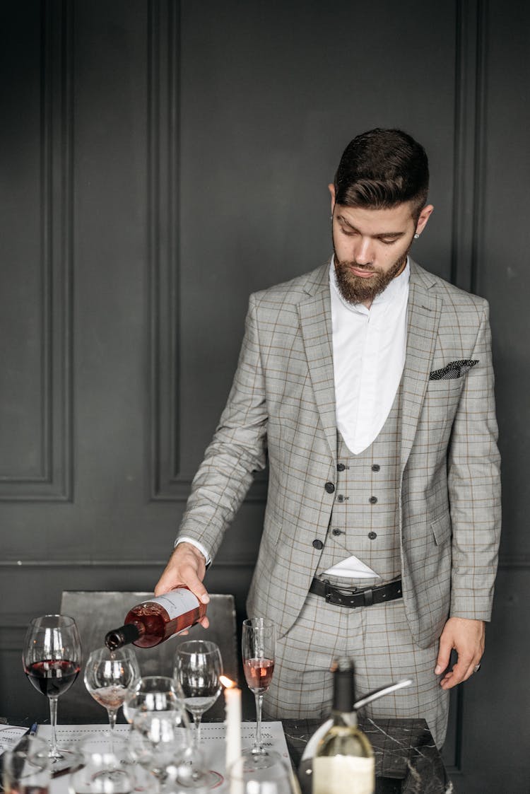 A Man In Plaid Suit Pouring The Red Wine On A Goblet Glass