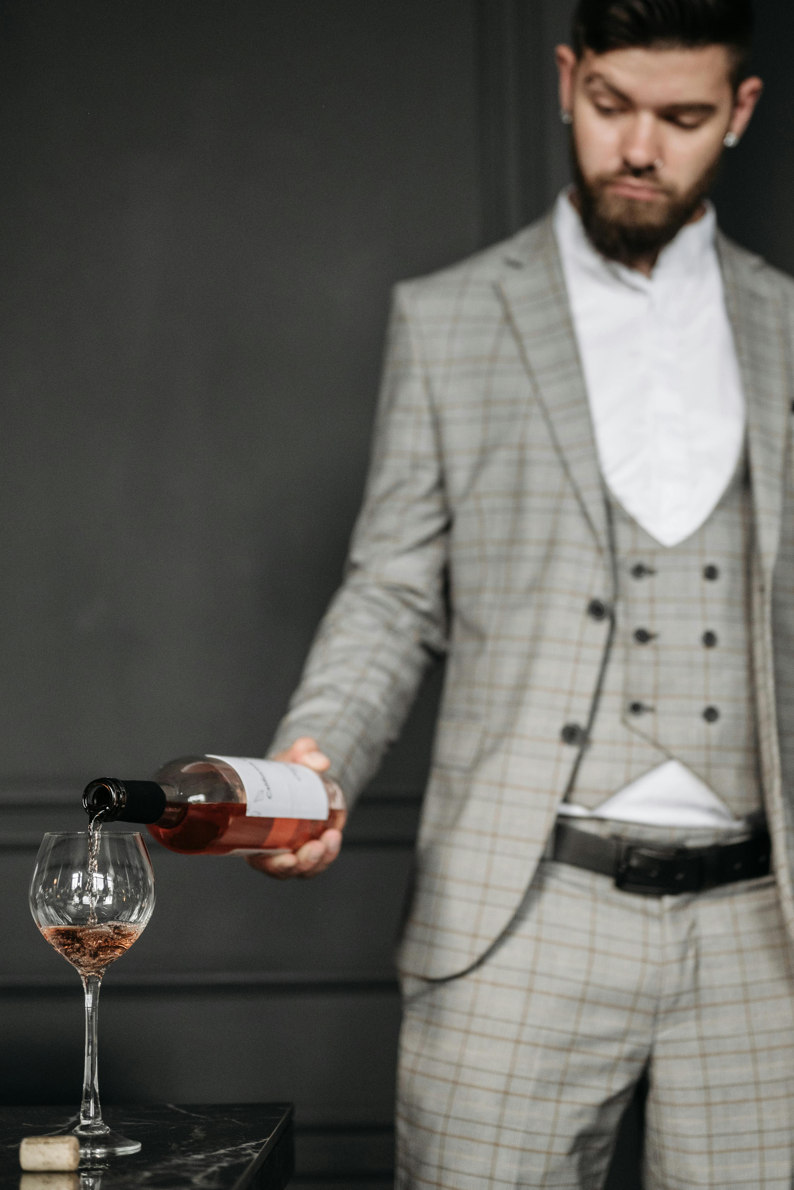 A stylish man in a suit pours rosé wine into a glass, highlighting sophistication and luxury.