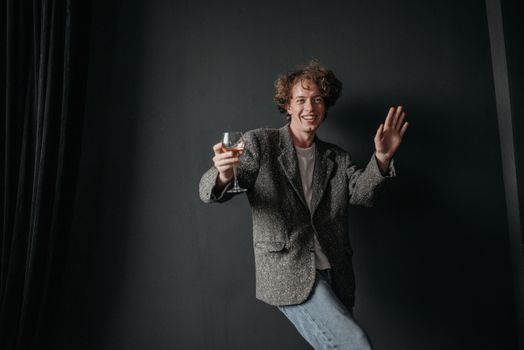 Man in a gray blazer joyfully holding a wine glass indoors with a dark background.