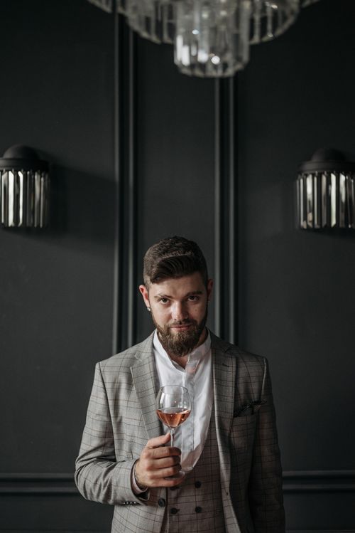 Free Sophisticated man in gray suit holding wine glass indoors against dark background. Stock Photo