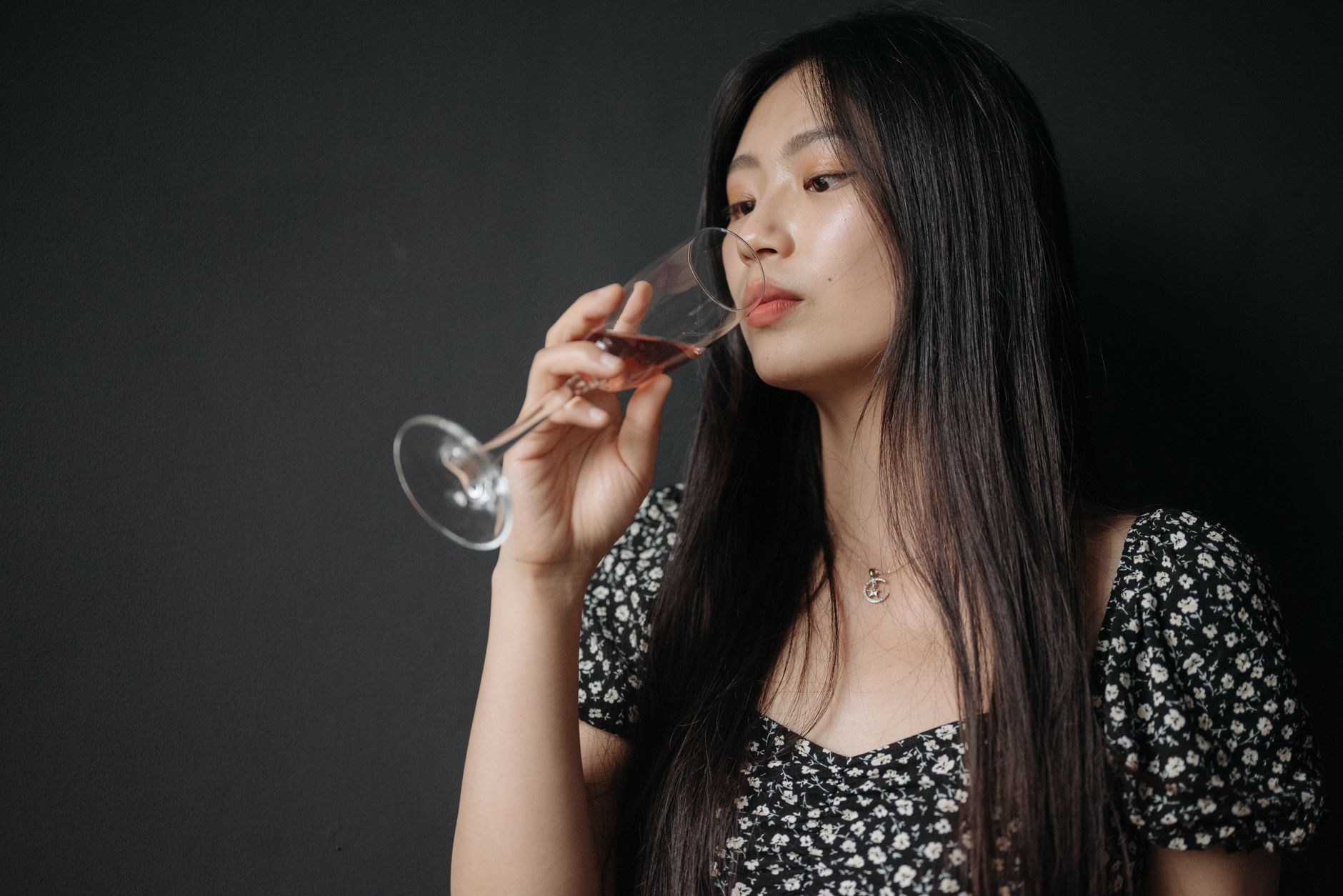 Elegant young woman enjoying a glass of red wine indoors, set against a stylish black backdrop.