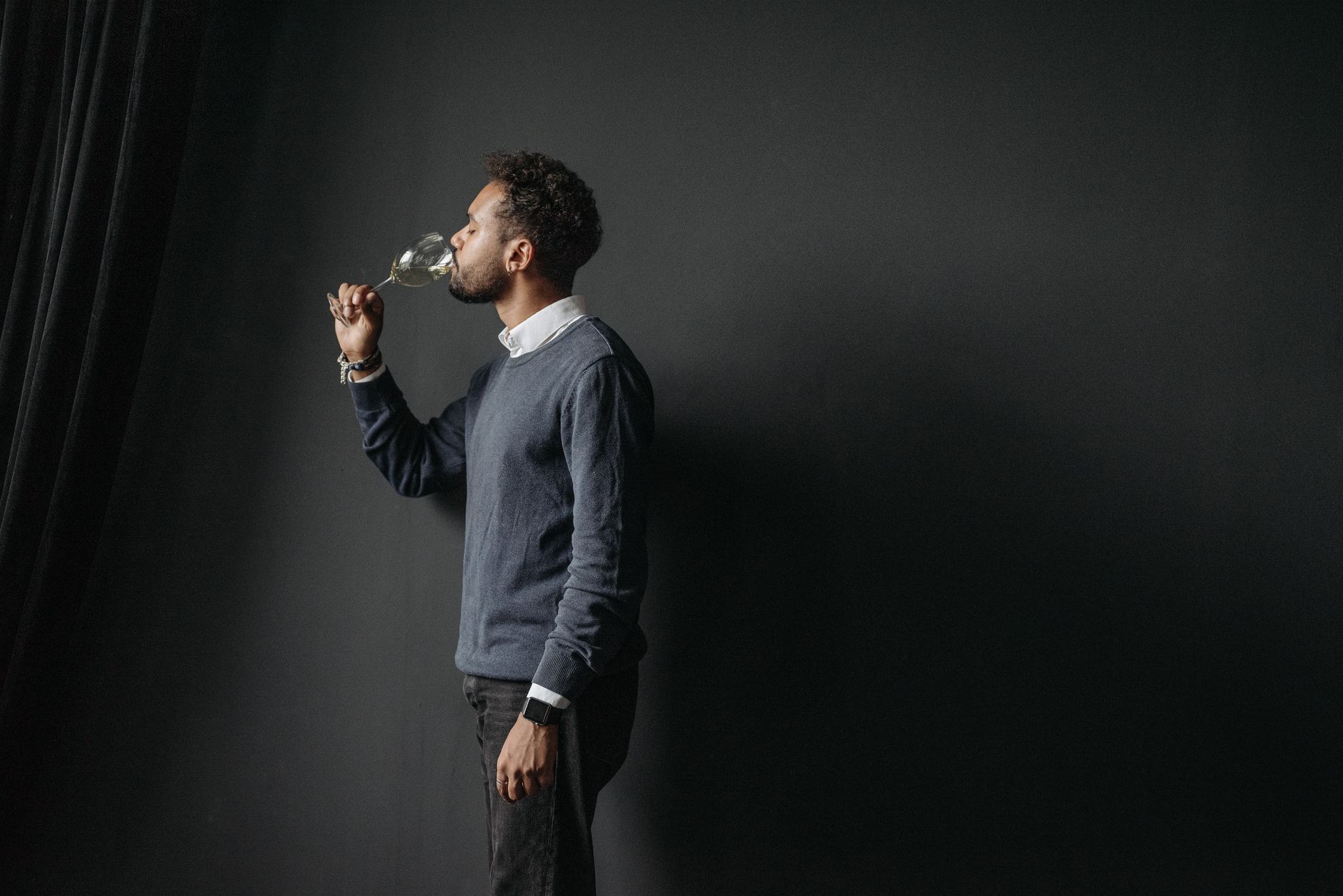 Profile of a man tasting white wine against a dark background, highlighting elegance.