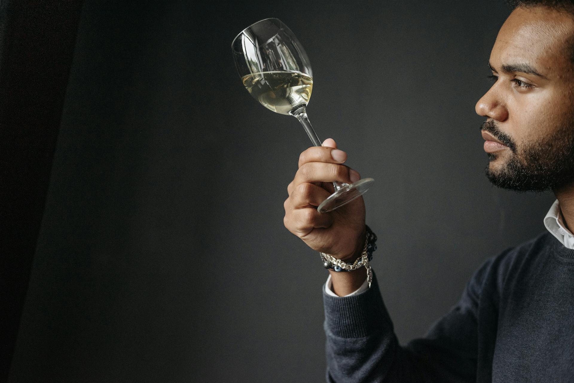 A man carefully examines a glass of white wine in a sophisticated atmosphere.