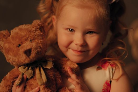 Charming close-up portrait of a young girl smiling and holding a teddy bear with a warm background.