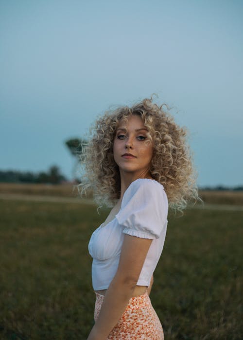 A Blonde Woman With Curly Hair Wearing a White Blouse 