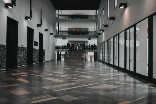 Free Spacious modern hall in Italy with people gathered around stairs, showcasing sleek architectural design. Stock Photo