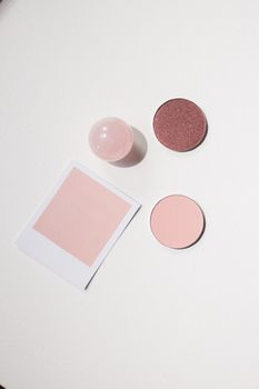 Minimalist flat lay of pink makeup products and objects on a white surface.