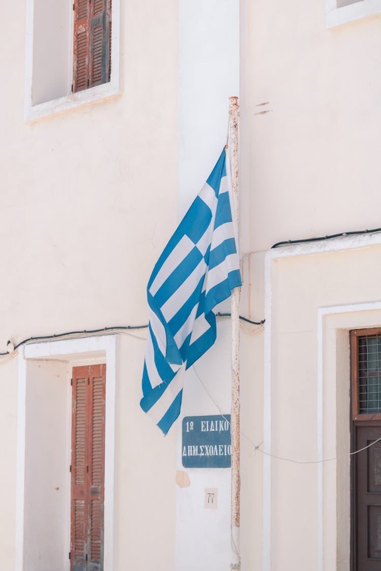 Flag Of Greece Swaying By The Wind Near White Building