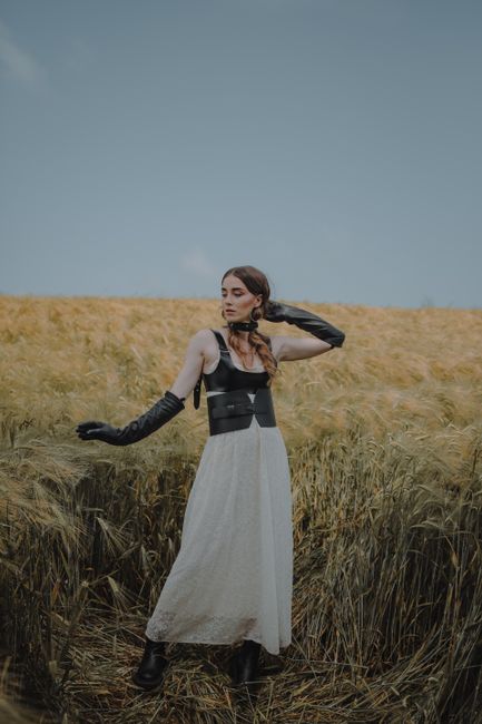 Woman in leather corset and gloves poses in a summer wheat field.
