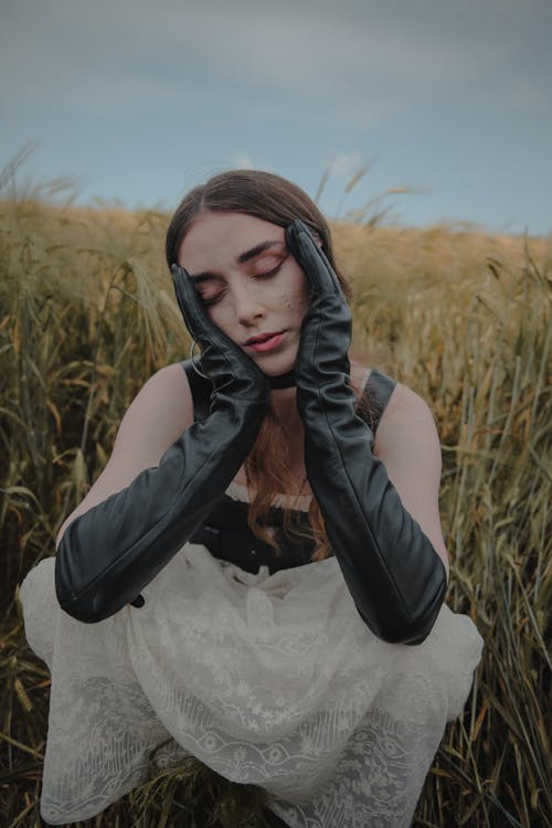 Free A Woman in Leather Gloves with Her Hands on Face Sitting on the Field Stock Photo