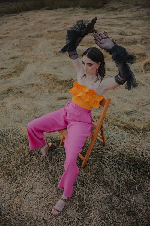 Woman Modeling Fashion Sitting on a Chair with her Arms Raised in a Field