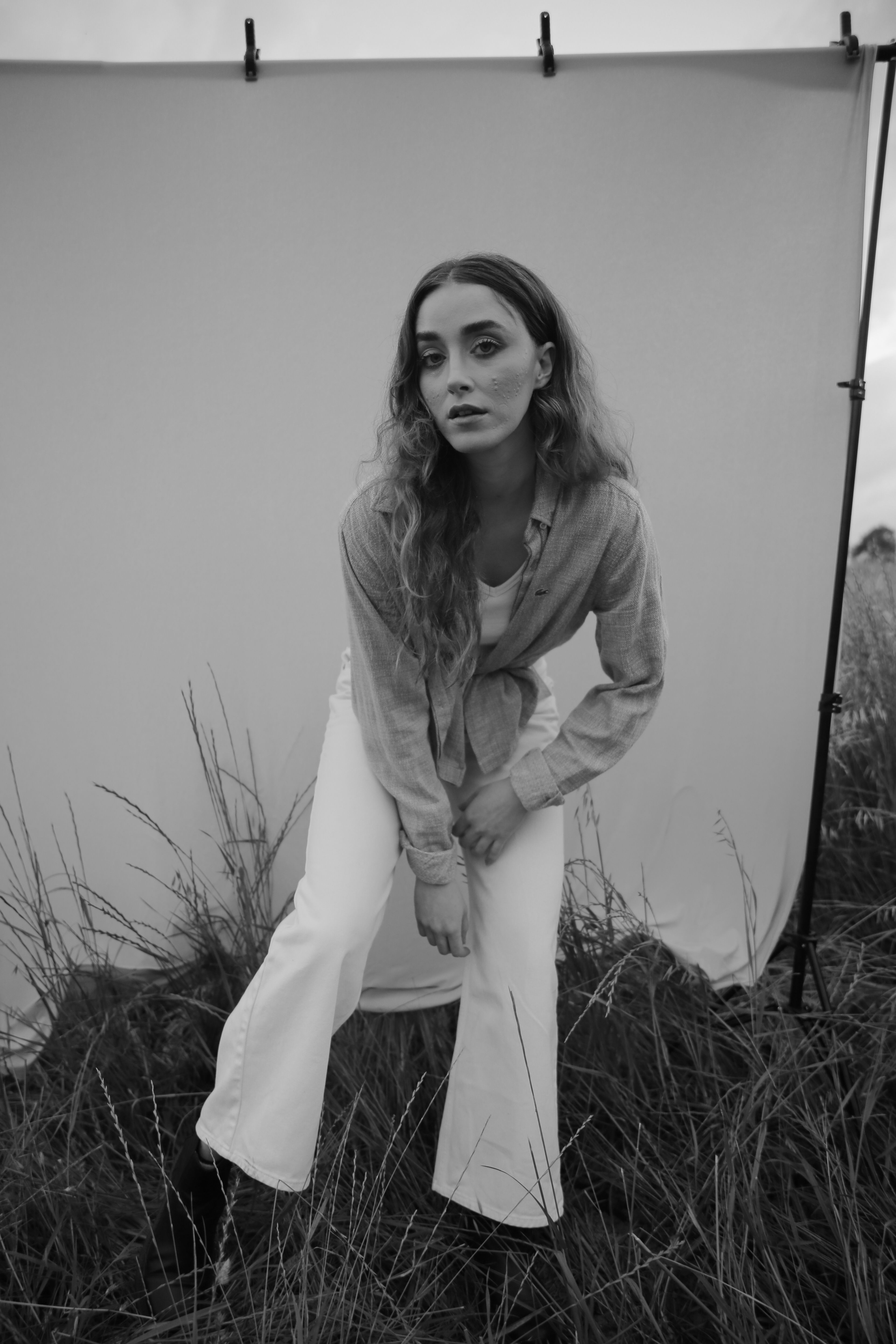 Artistic black and white portrait of a woman posing in a field with a fabric backdrop.