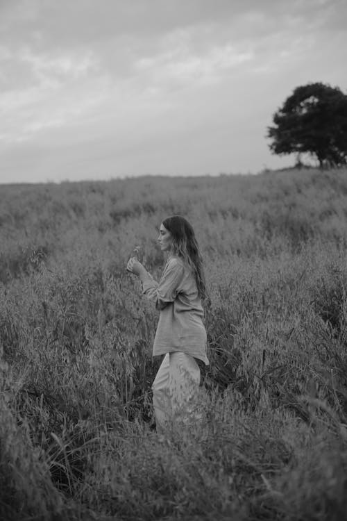 Grayscale Photo of Woman Holding a Flower in the Middle of a Field