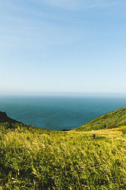 Free A peaceful coastal landscape featuring grassy hills and a calm sea under a clear blue sky. Stock Photo