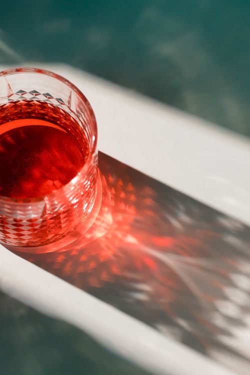 Free Crystal glass with a red liquid casting artistic shadows on a surface in sunlight. Stock Photo