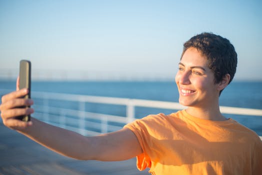 A cheerful young woman in an orange shirt takes a selfie by the seaside in Portugal.