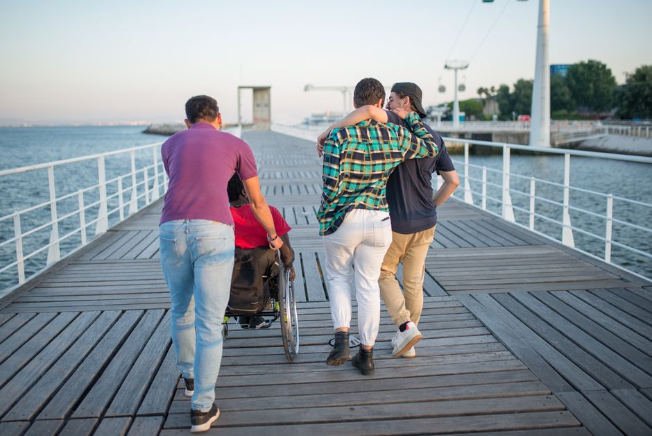 Grupo de amigos caminando a lo largo de un pintoresco paseo marítimo junto al mar, promoviendo la amistad y la accesibilidad.