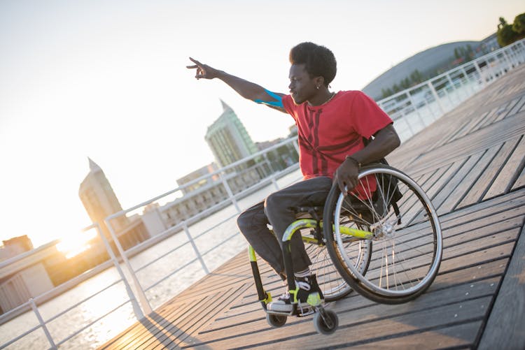 Black Man Sitting In Wheelchair On Pier On Sunset