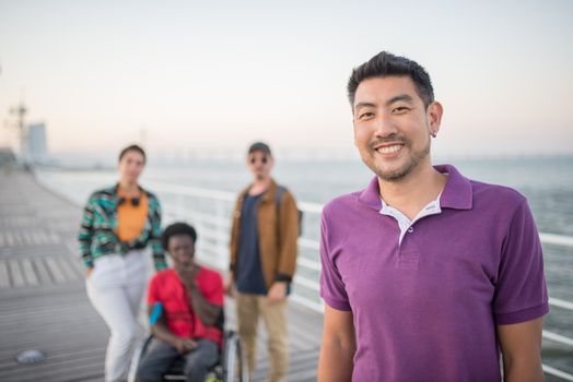 A diverse group of friends smiling together on a seaside boardwalk in Lisbon, Portugal during the day.