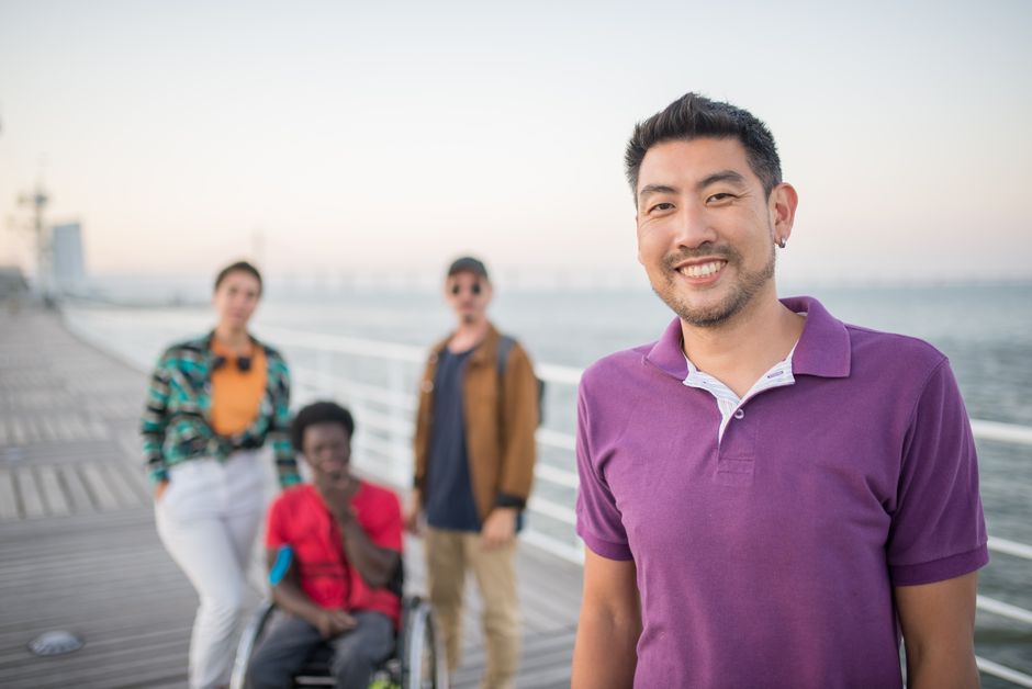 A diverse group of friends smiling together on a seaside boardwalk in Lisbon, Portugal during the day.