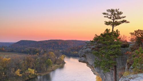 Free Breathtaking view of a river winding through a forest with a dramatic cliff at sunset. Stock Photo