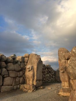 Stone statues at the Lion Gate of Hattusa, Türkiye with dramatic clouds overhead.