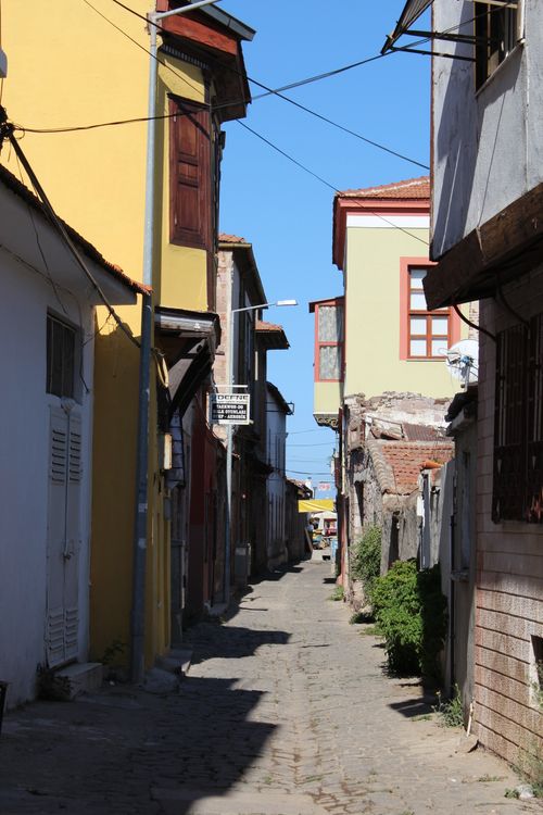 Free Explore the historic charm of Ayvalik with this vibrant alleyway view, showcasing colorful buildings under the clear sky. Stock Photo