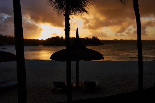 A tranquil beach scene at sunset with a silhouetted parasol against a colorful sky.