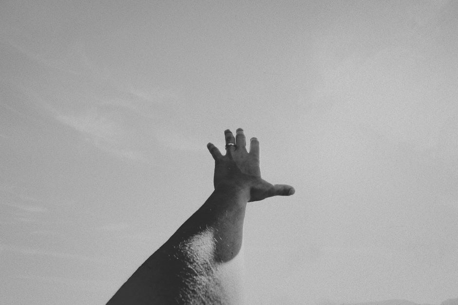 Artistic black and white image of a hand reaching towards the sky, symbolizing aspiration.