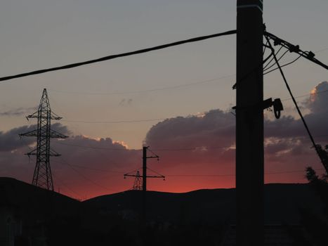 Electric poles silhouetted against a stunning sunset with vibrant colors and dynamic cloud formations.