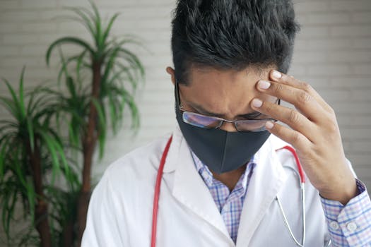 A thoughtful doctor wearing eyeglasses and mask indoors, appearing concerned.