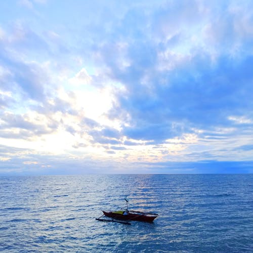 Blue Image of a Boat on an Ocean and Cloudscape