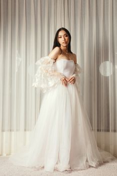 Beautiful Asian bride posing in an elegant lace wedding gown indoors.