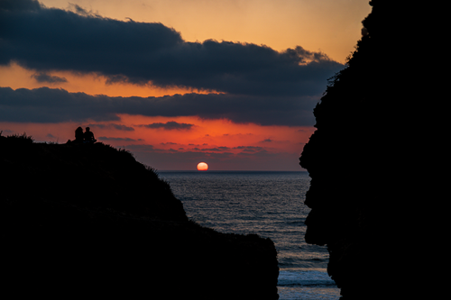 Free Silhouetted couple watching a beautiful sunset over the ocean with dramatic clouds. Stock Photo