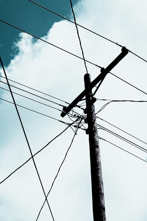 Free Low-angle view of power lines on a wooden post against a blue sky with clouds. Stock Photo