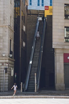 Escalator between modern buildings in Lleida, Spain, with people using it on a sunny day.