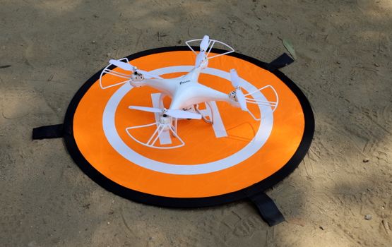 A white quadcopter rests on an orange landing pad on sandy ground.