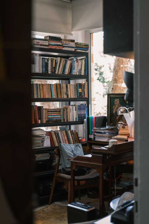 Free A warm home library featuring a filled bookshelf, wooden desk, and window view. Stock Photo