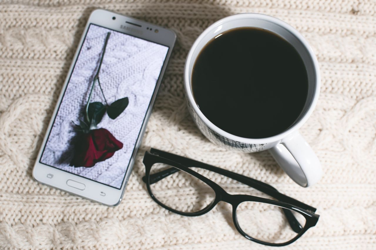 a cozy flat lay featuring coffee smartphone with rose image and eyegla