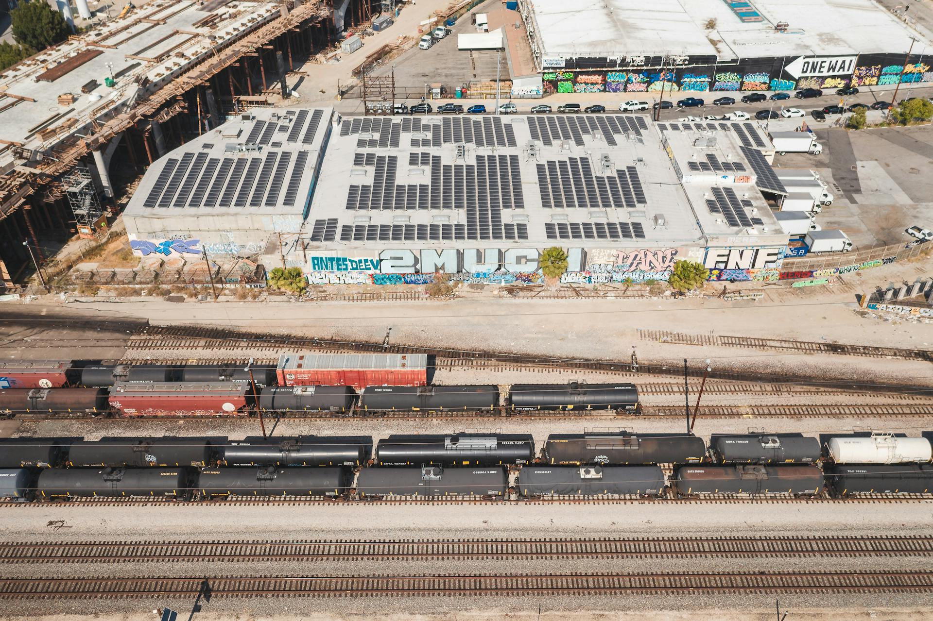 Aerial view of railroad tracks beside urban buildings with graffiti and solar panels.